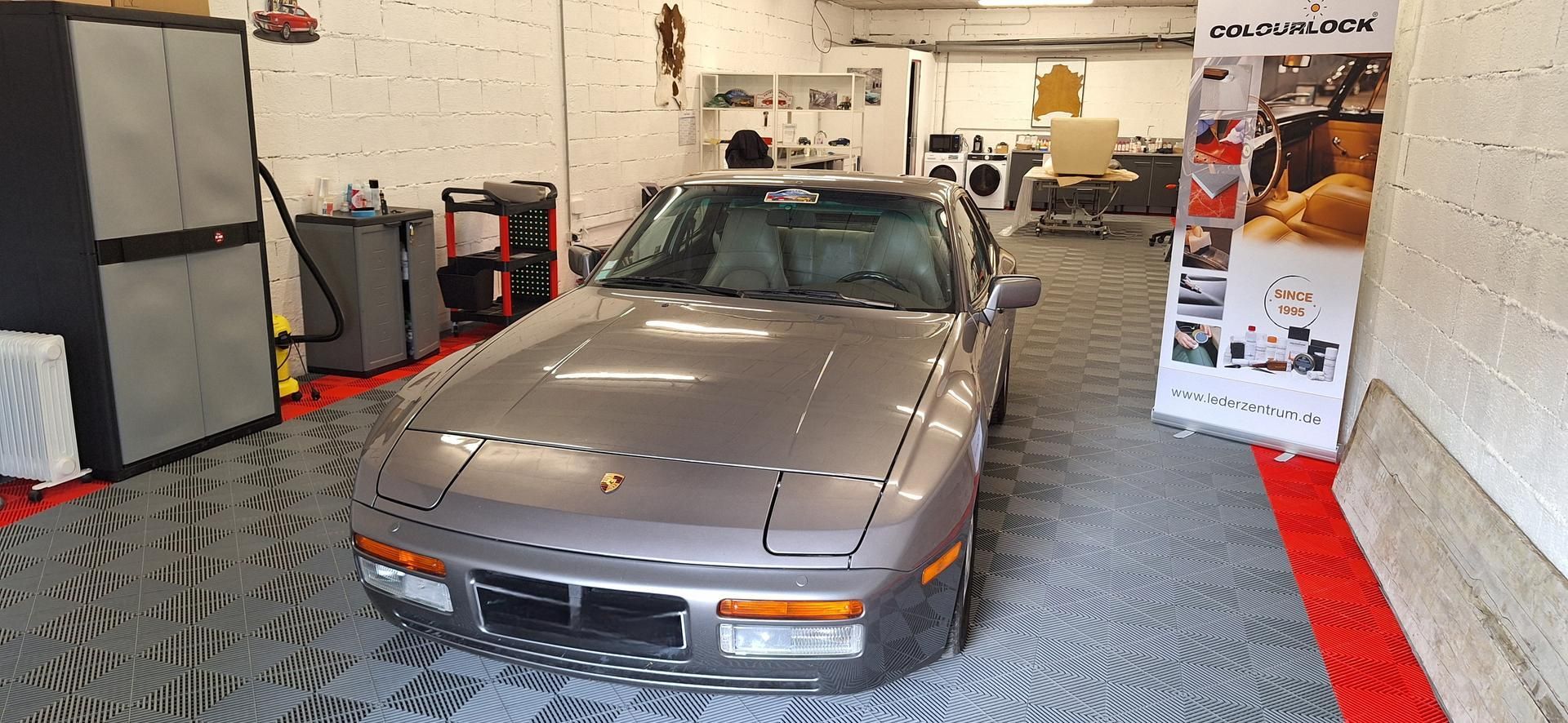 Porsche 944 argentée garée dans un garage avec armoires et équipements.