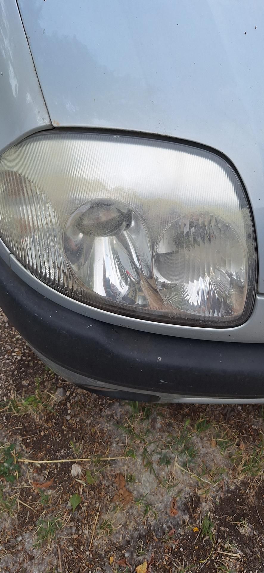 Phare d'une voiture argentée, avec une lentille trouble et une garniture noire.