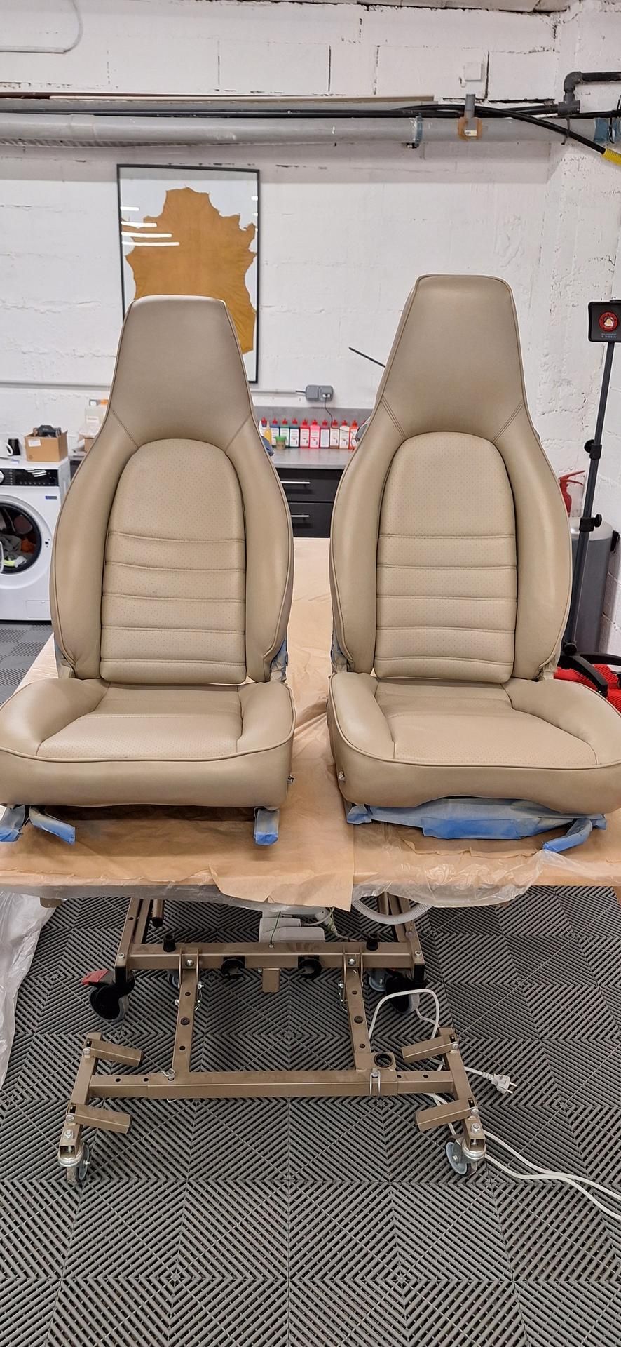 Deux sièges auto beiges sur un pont élévateur. Ils se trouvent dans un garage fermé.