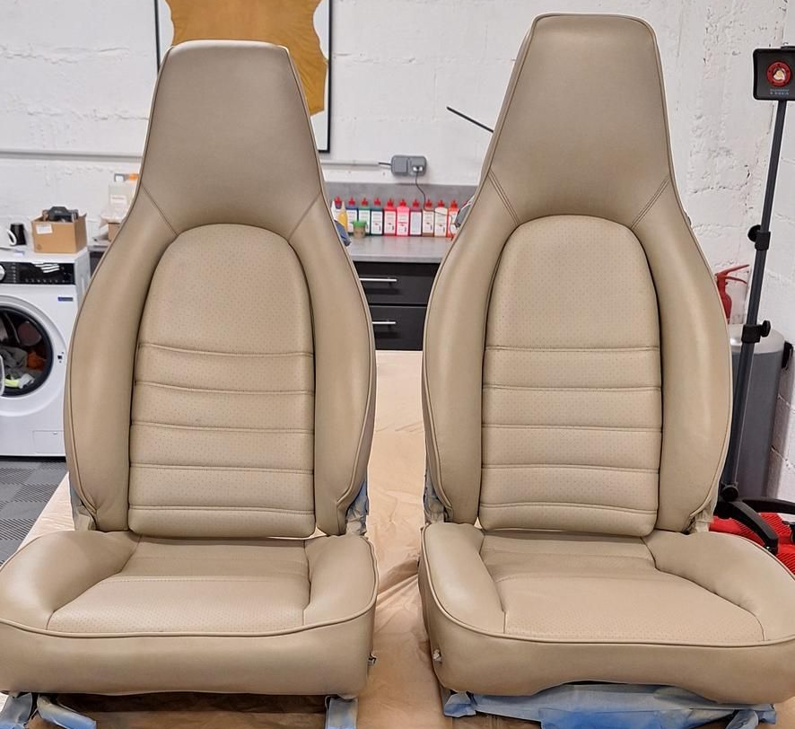 Deux sièges auto beiges sur un support à roulettes dans un atelier.