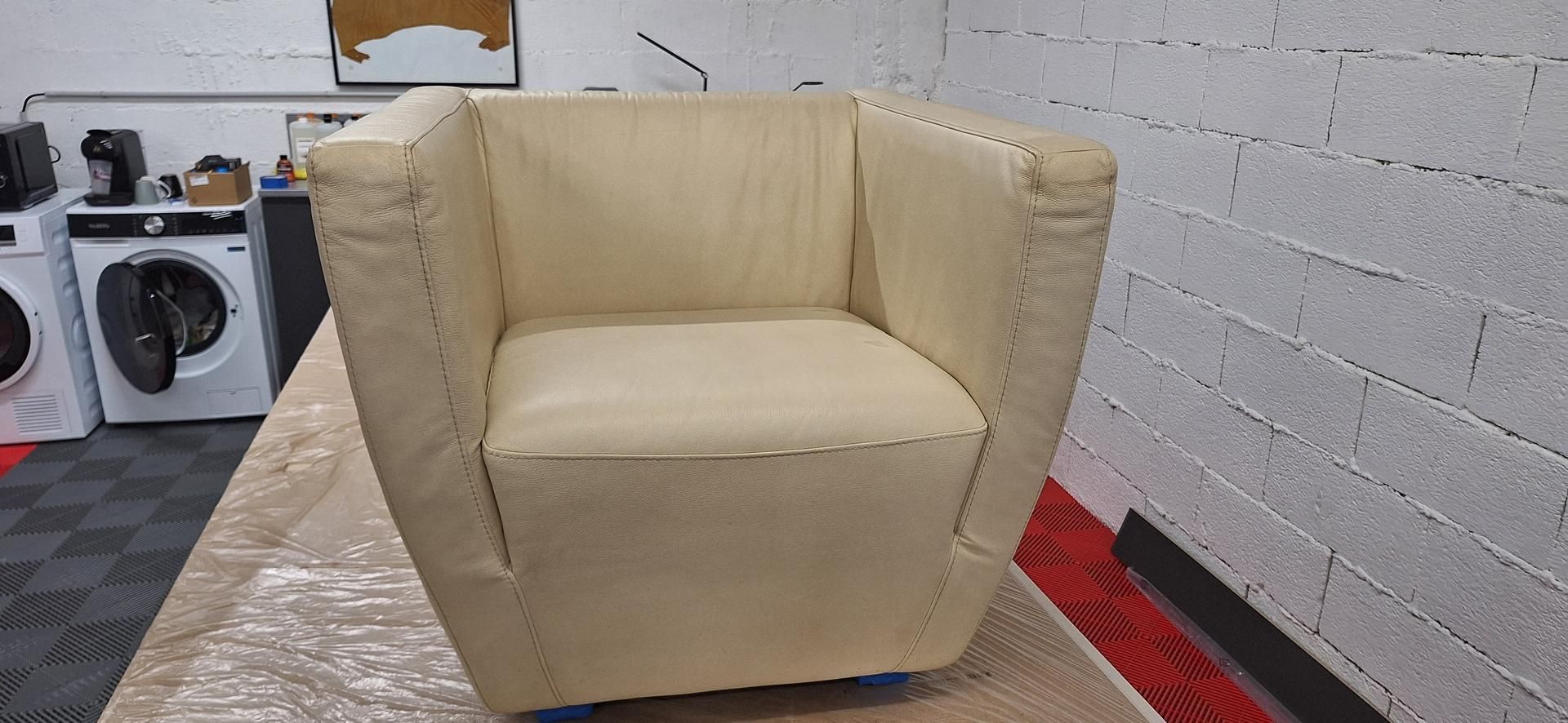 Un fauteuil de couleur crème est posé sur une surface, contre un mur de briques blanches et à proximité d'appareils électroménagers.