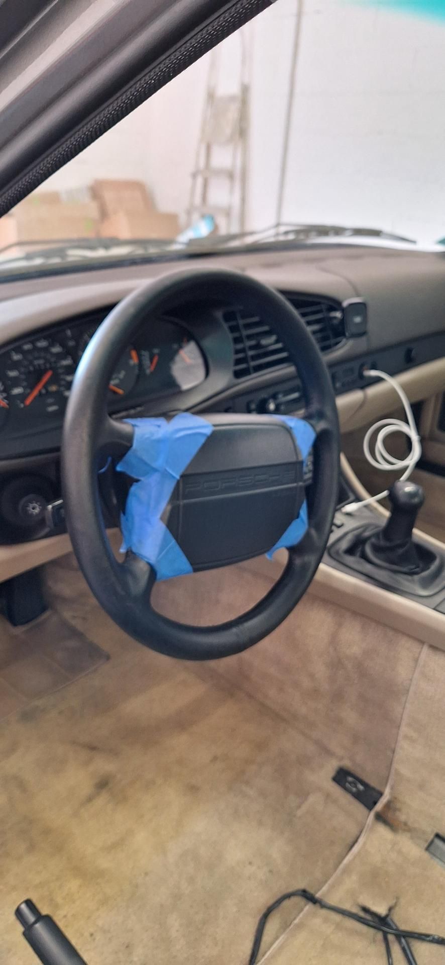 Intérieur d'une voiture ancienne avec volant noir recouvert de ruban adhésif bleu. Un levier de vitesses est visible.