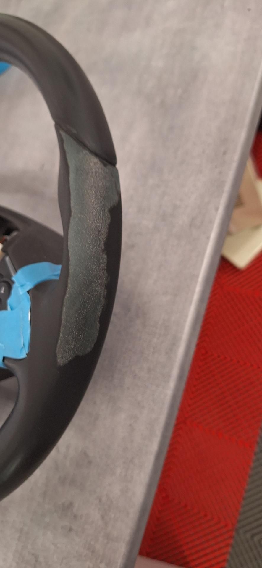 Volant noir endommagé avec ruban adhésif gris décollé. Peinture bleue sur le volant. Posé sur une surface grise.