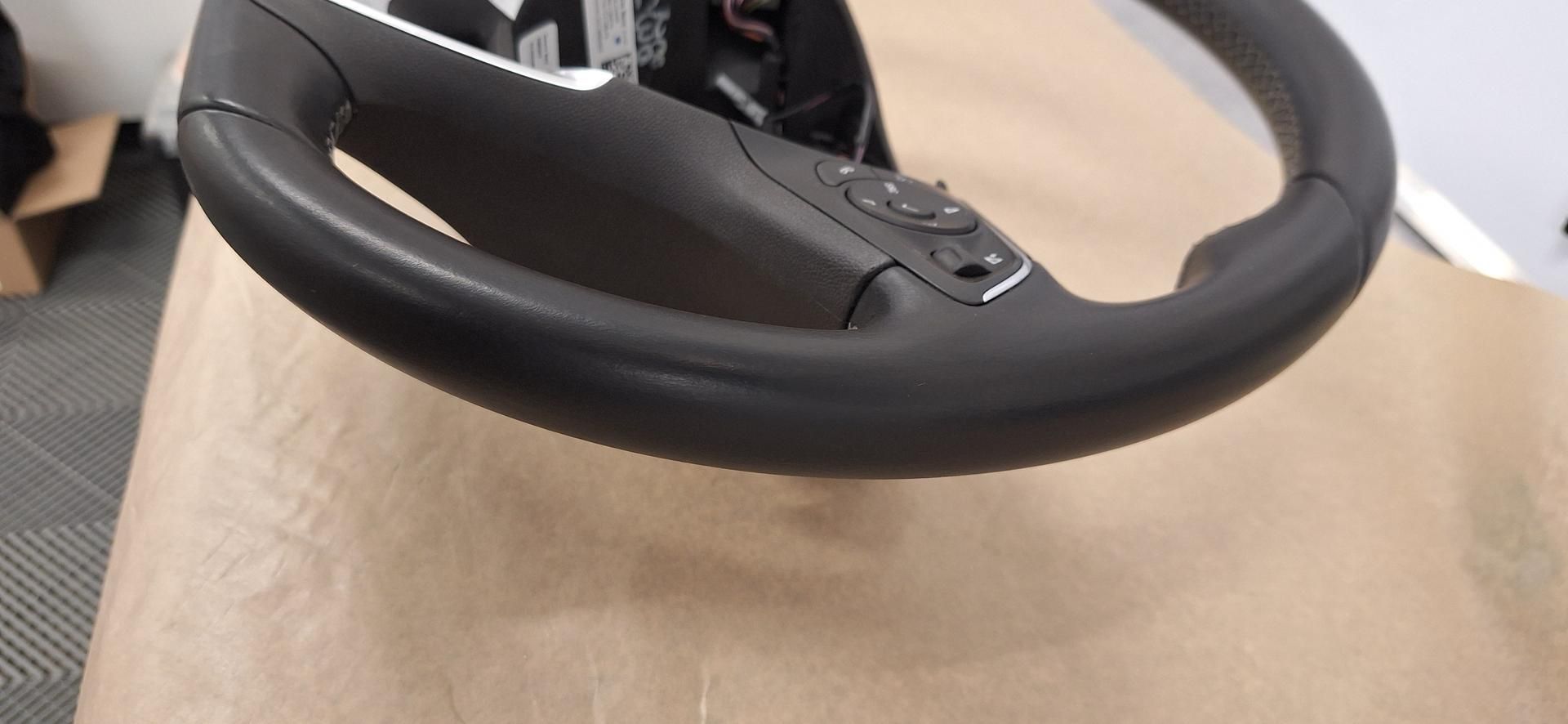 Gros plan sur un volant noir avec des boutons, sur une surface marron clair.