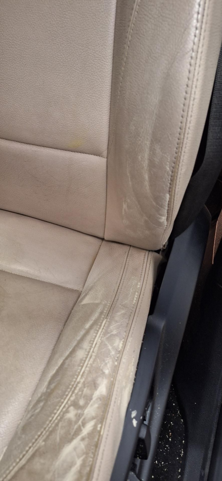 Siège auto en cuir beige avec usure visible, vue rapprochée.