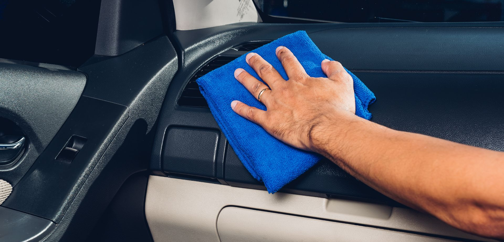Personne nettoyant le tableau de bord d'une voiture avec un chiffon bleu.