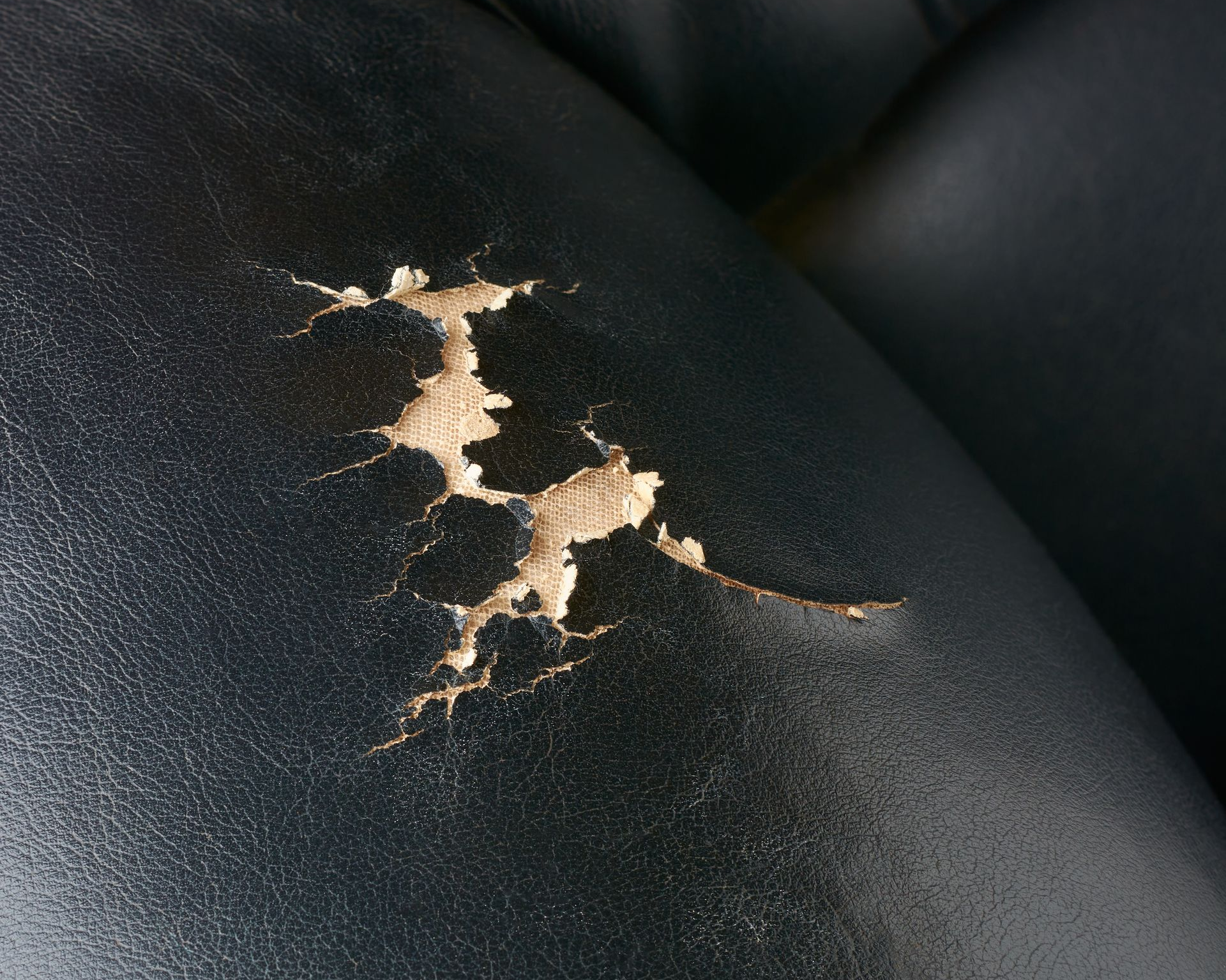 Siège en cuir noir avec de grandes déchirures exposant le matériau sous-jacent.