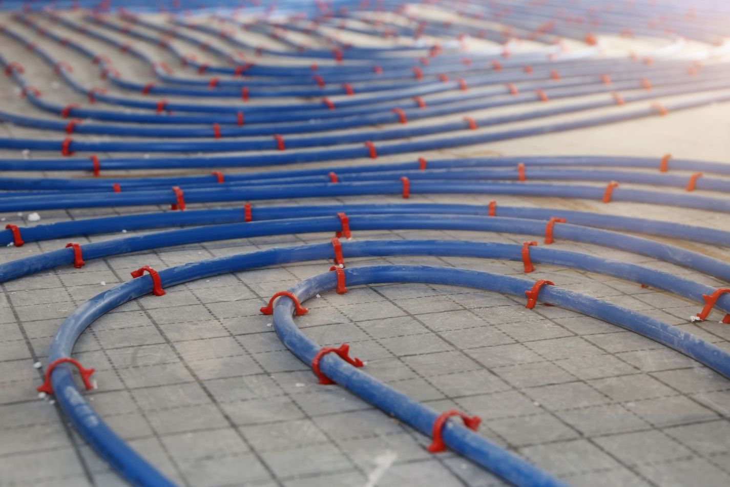 Tubes de chauffage radiant bleus fixés sur une grille au sol en béton, prêts à être installés.
