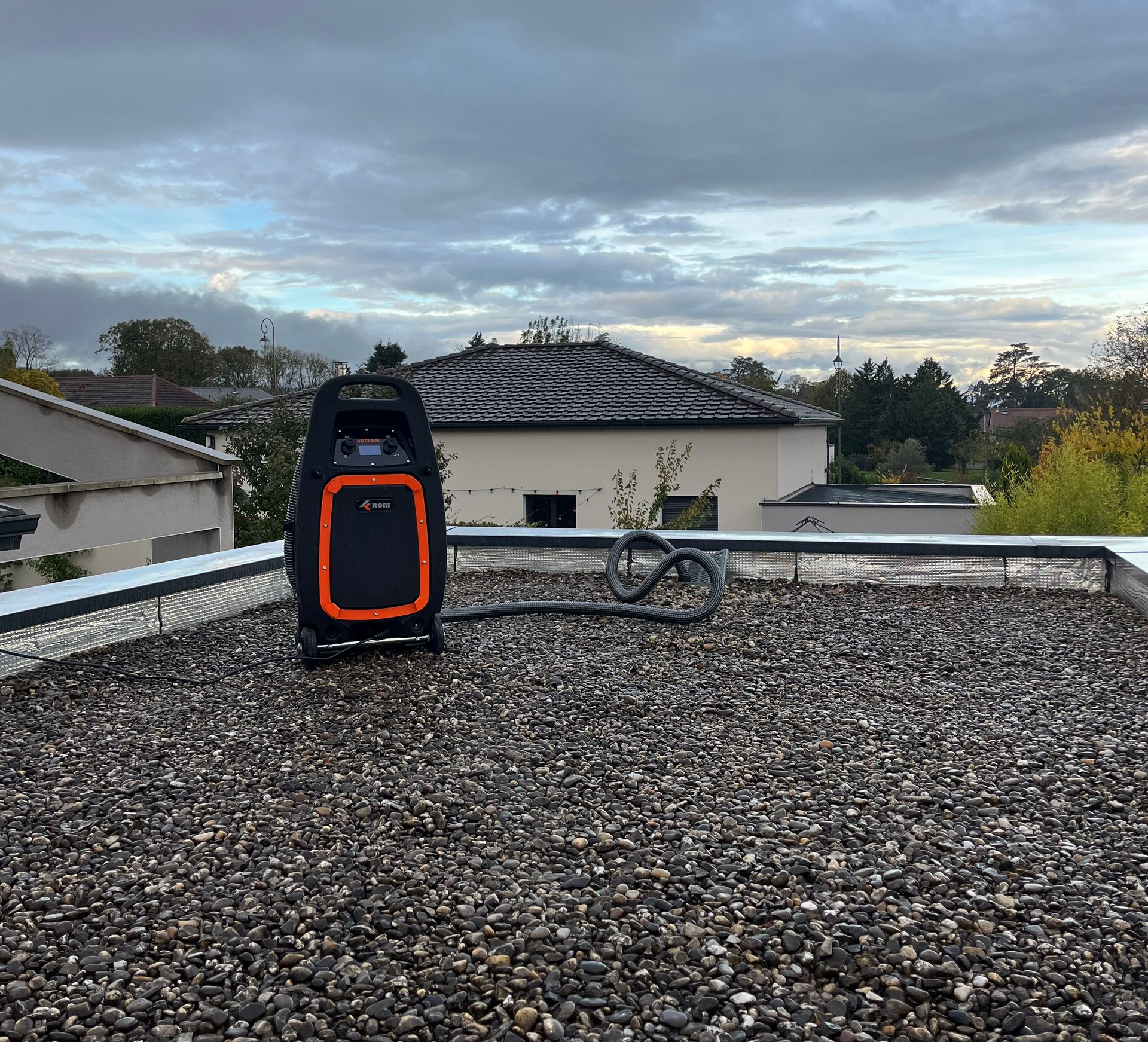 Matériel de recherche de fuite avec un tuyau est installée sur un toit recouvert de gravier, sous un ciel couvert.