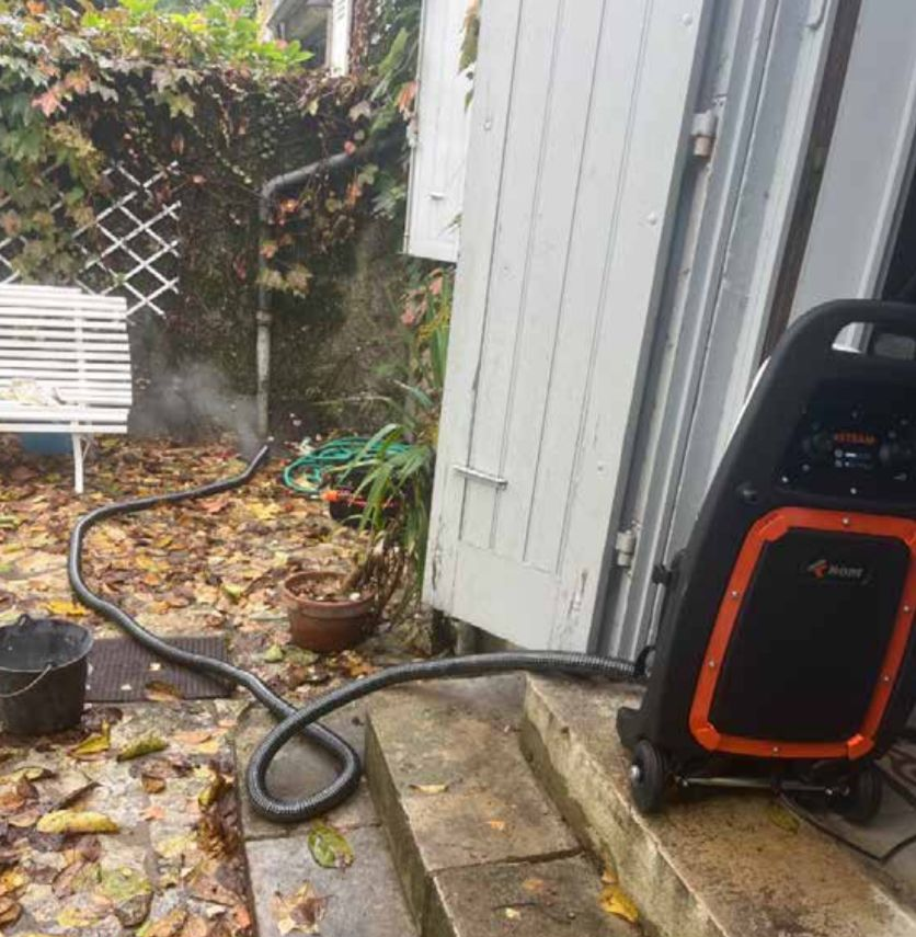 Matériel de recherche de fuite dans un jardin, tuyau branché, en fonctionnement, près d'une porte.