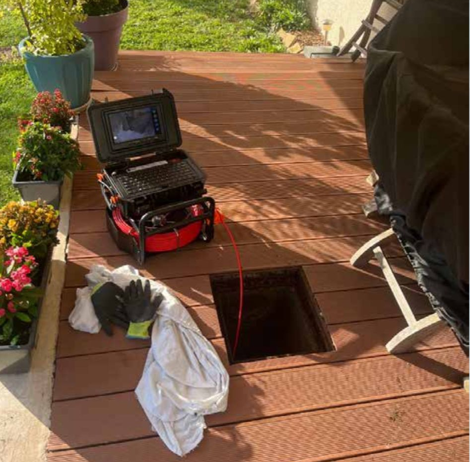 Du matériel de caméra est installé sur le pont, inspectant un point d'accès ouvert. Un câble rouge s'étend dans l'ouverture.