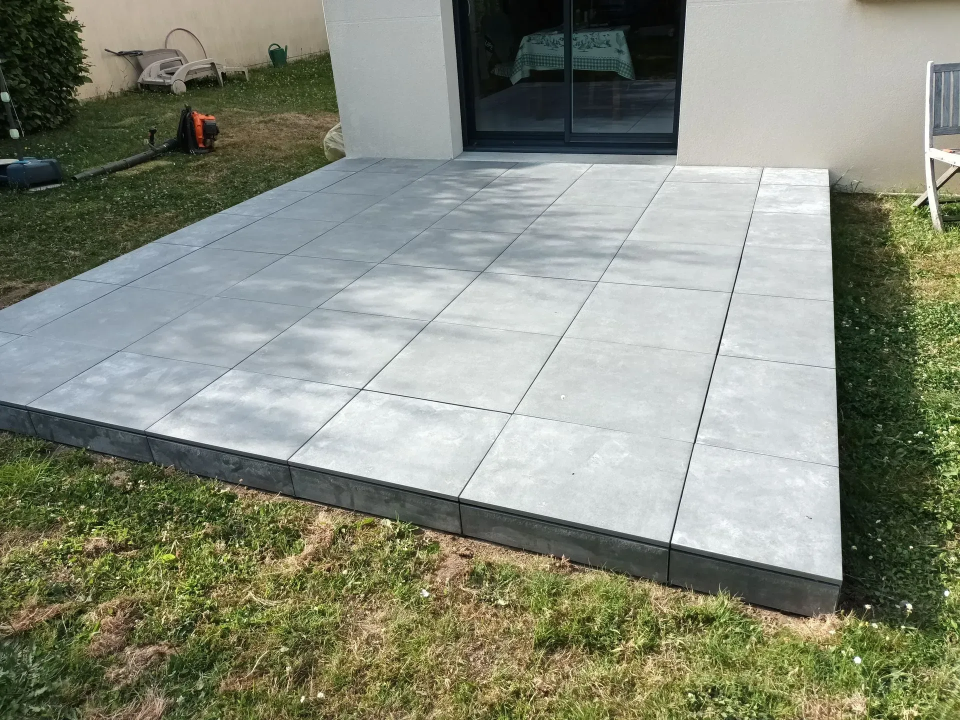 Patio en pierre grise à l'extérieur d'une maison avec de l'herbe sur les côtés.