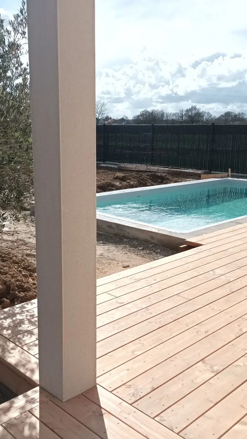 Pilier blanc à côté d'une terrasse en bois, d'une piscine et d'un ciel couvert au loin.