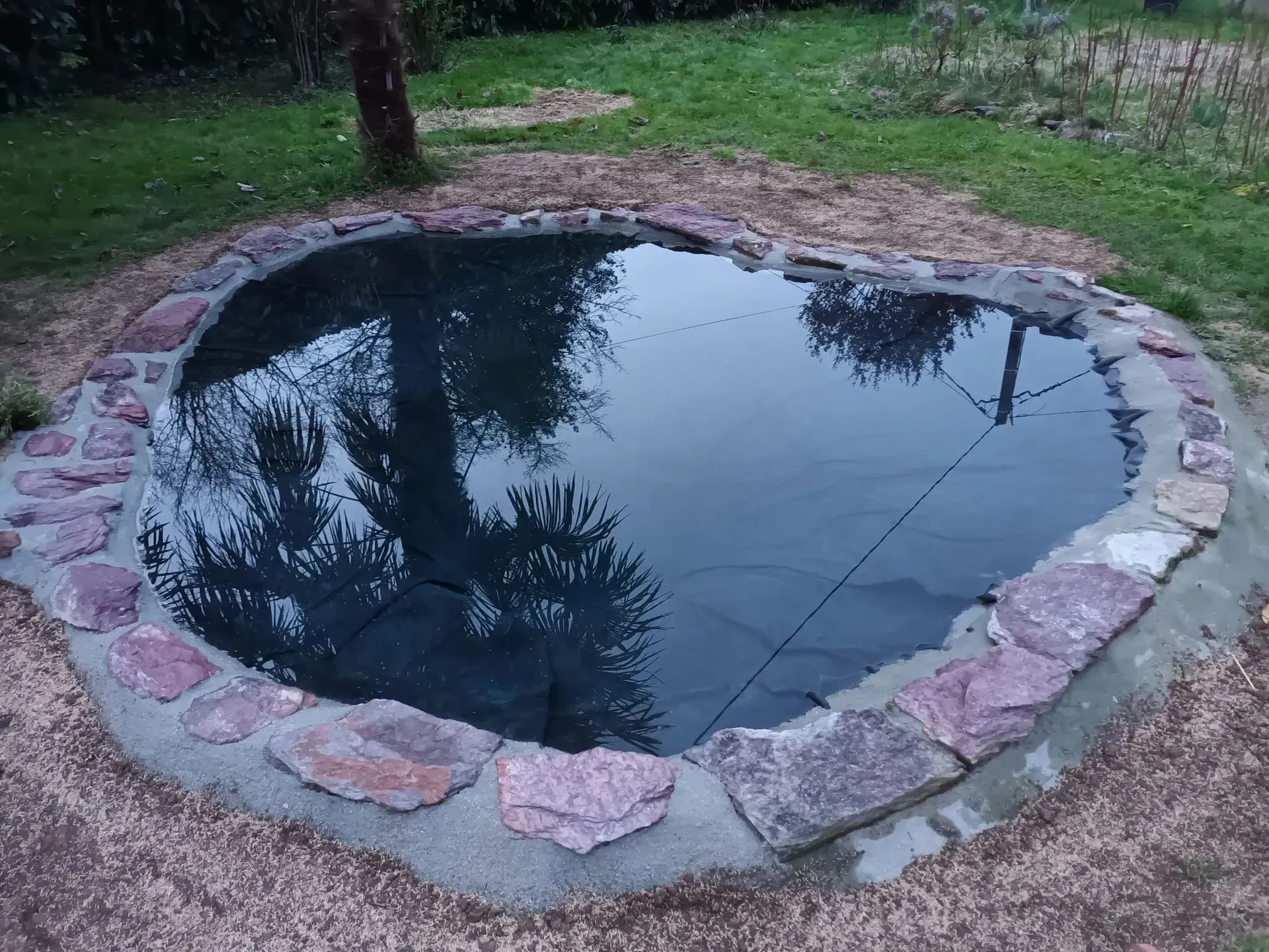 Un petit étang bordé de rochers reflétant les arbres et le ciel.