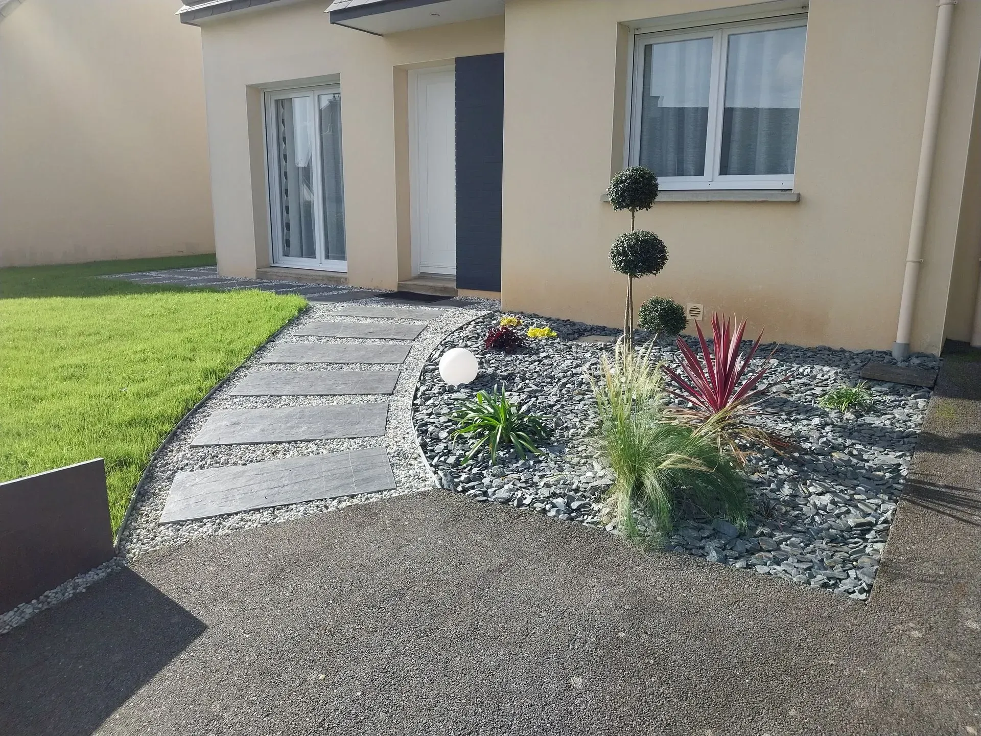 Chemin en pierre menant à une maison beige avec aménagement paysager.