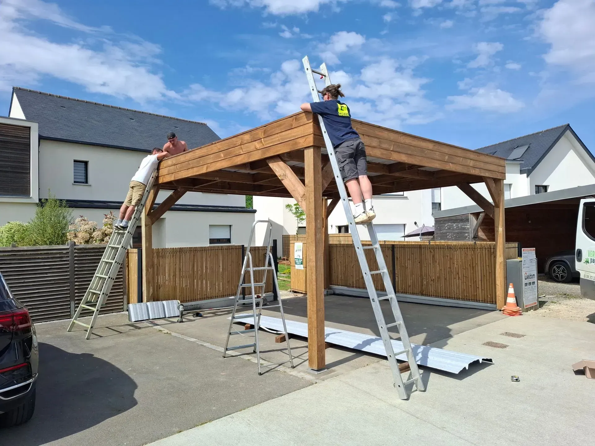 Des gens construisent une pergola en bois dans une allée. Deux personnes sur des échelles travaillent sur le toit.