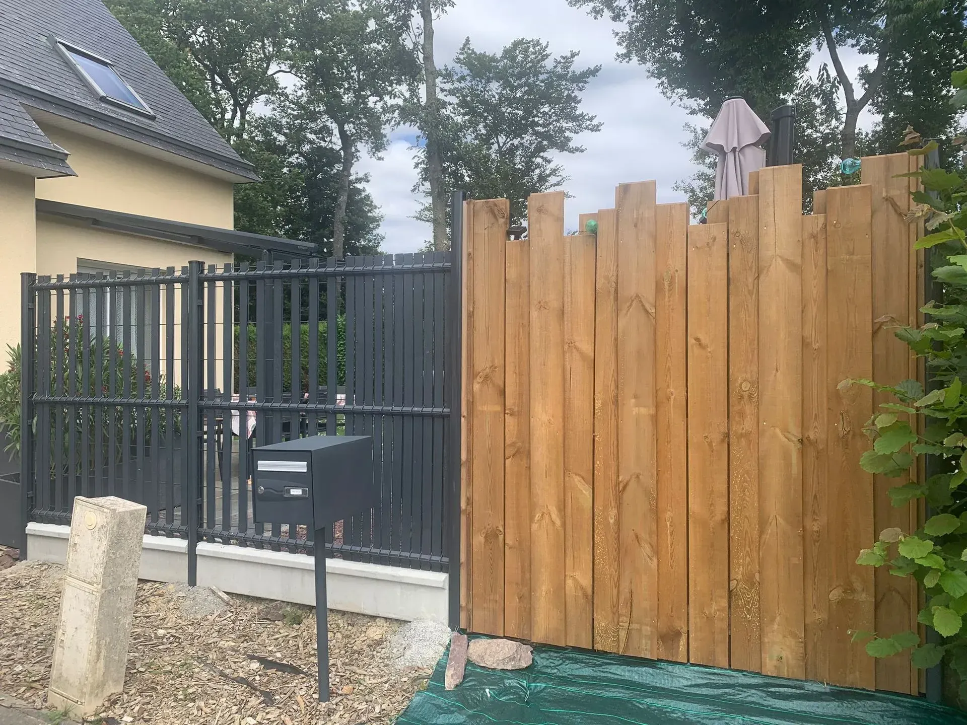 Clôture en bois et portail en métal noir à côté d'une maison et d'une allée en gravier.