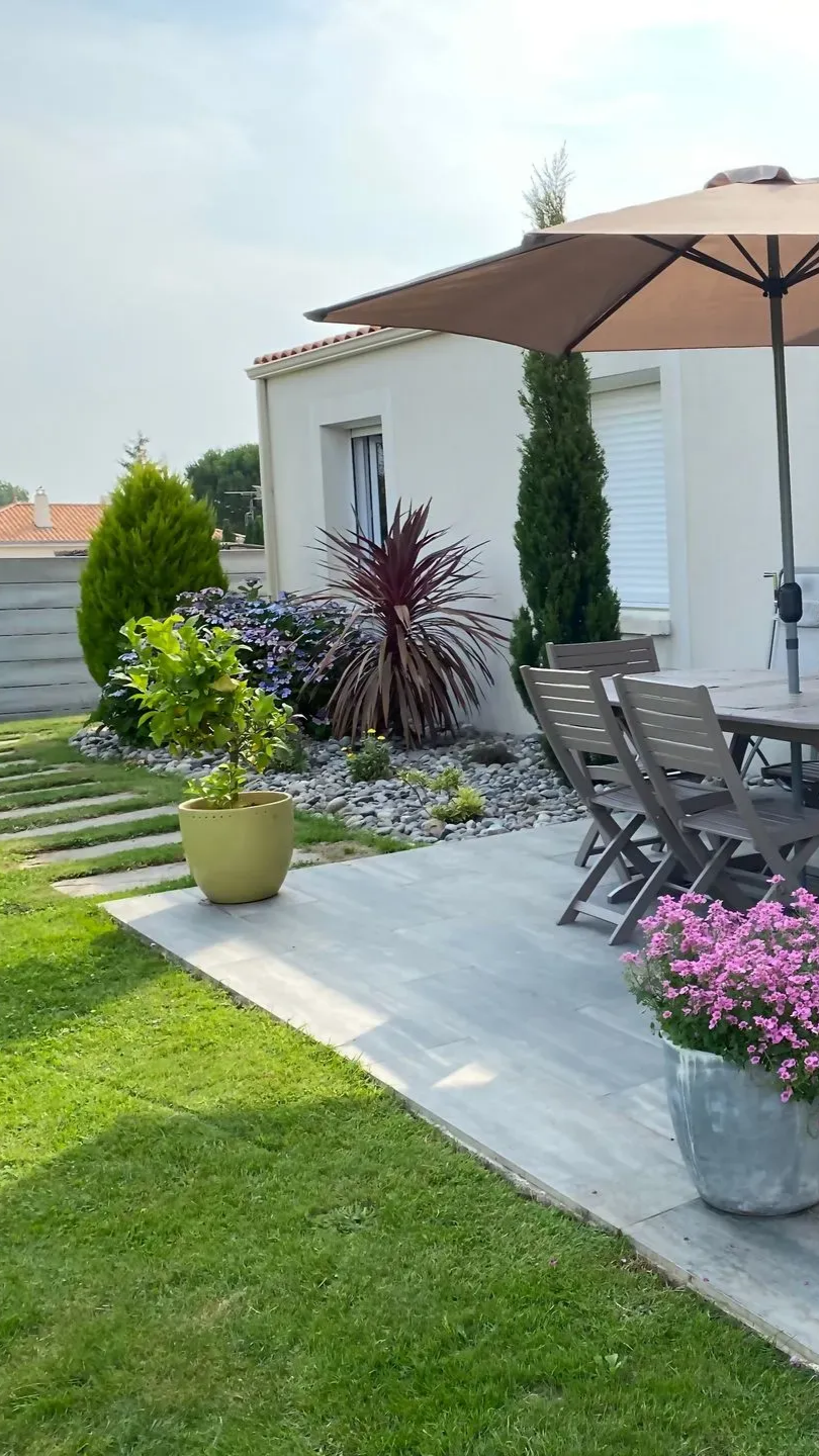 Arrière-cour avec maison, meubles de patio, plantes en pot et jardin paysager.