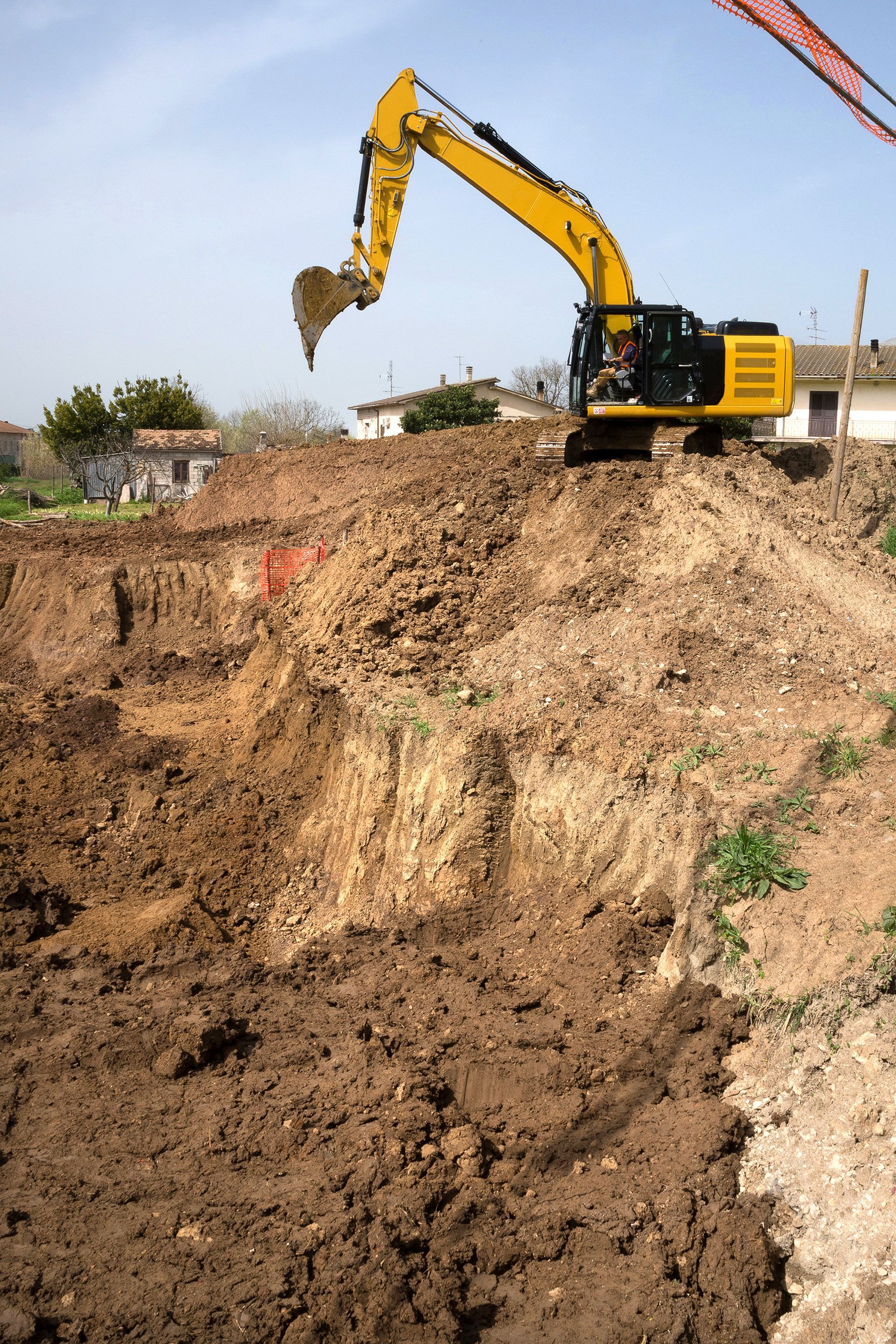 Excavatrice jaune creusant une tranchée dans un chantier de construction en terre.