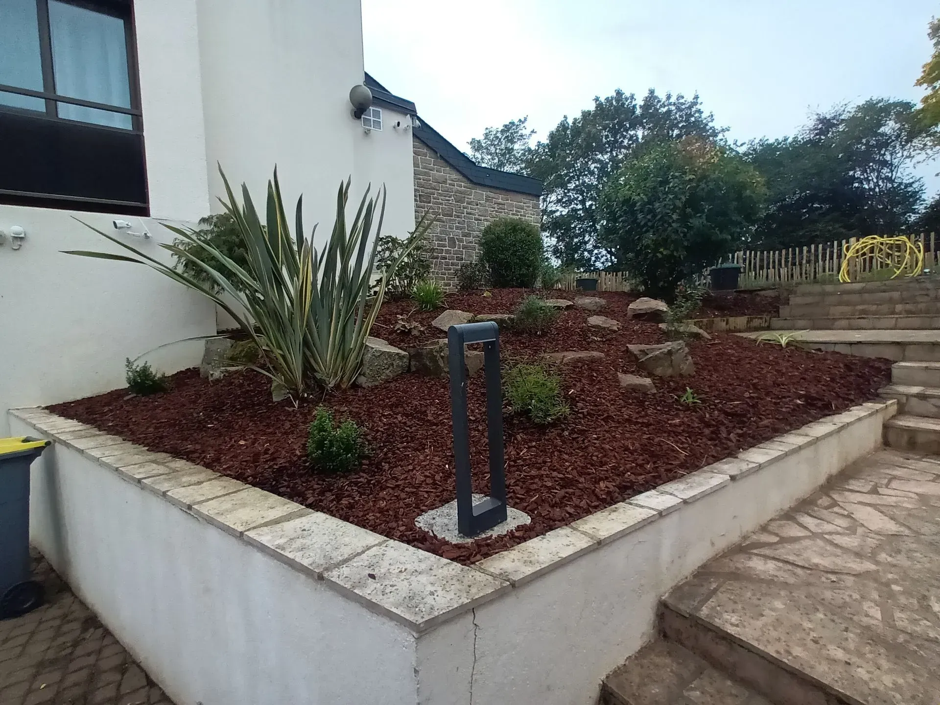 Un jardin paysager moderne avec paillis, rochers et plantes devant une maison.