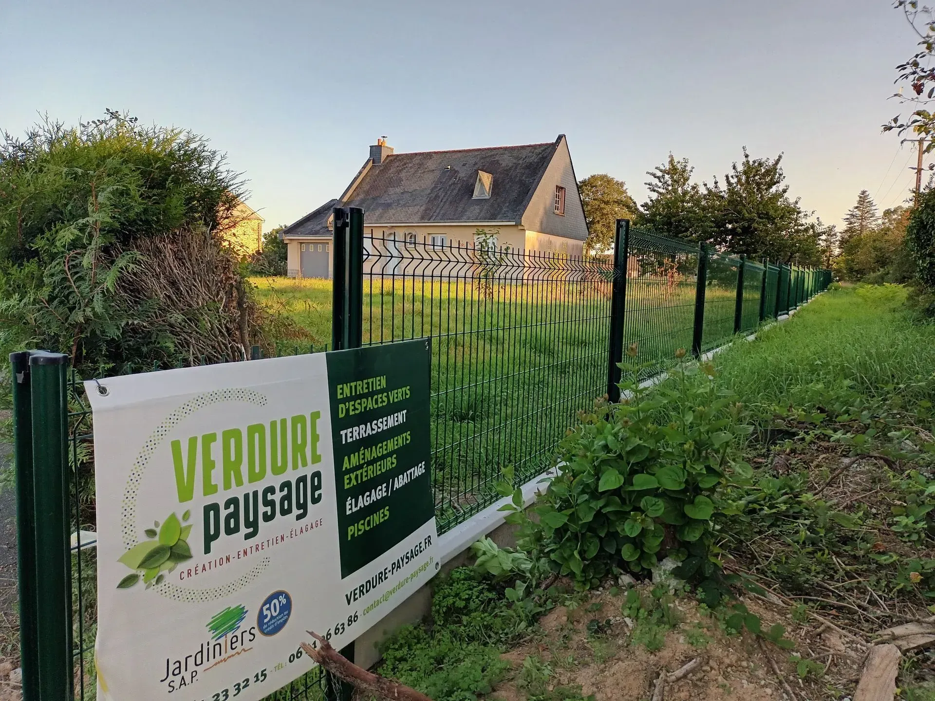 Panneau Verdure Paysage à proximité d'une maison, avec une clôture et une végétation verte.