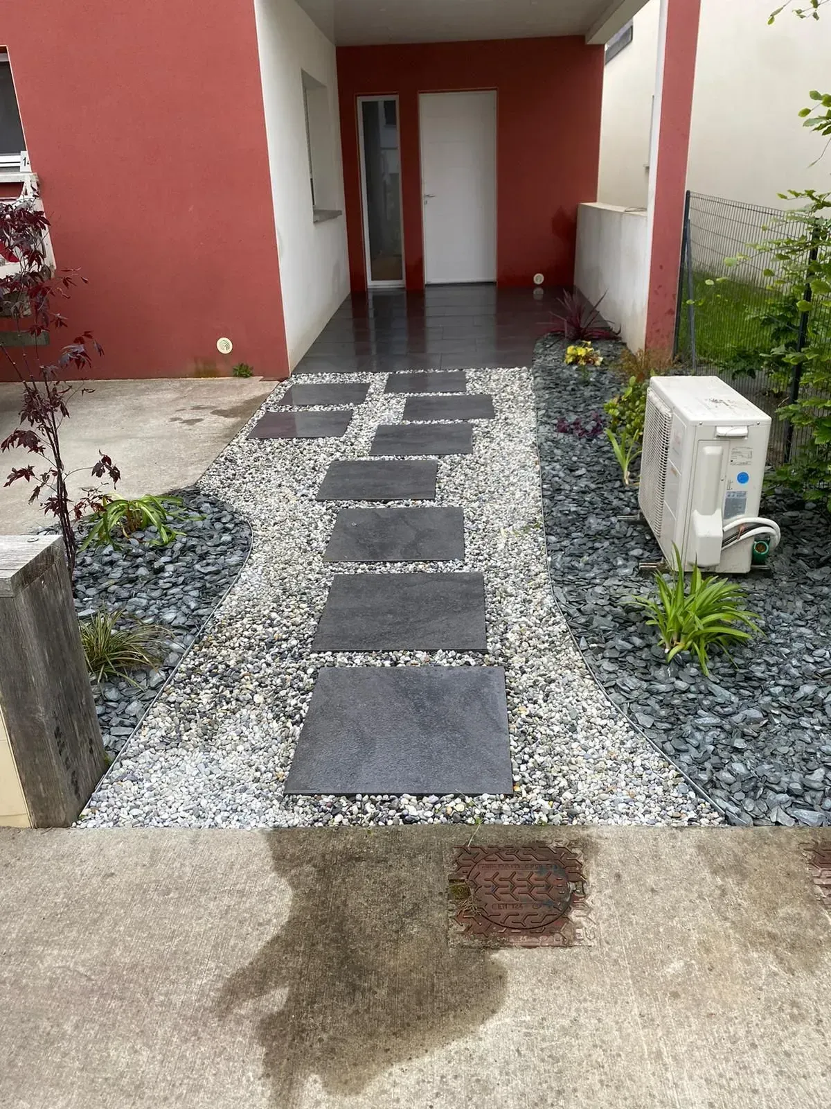 Chemin en pierre avec des pas japonais menant à une porte, entouré de gravier et de plantes.