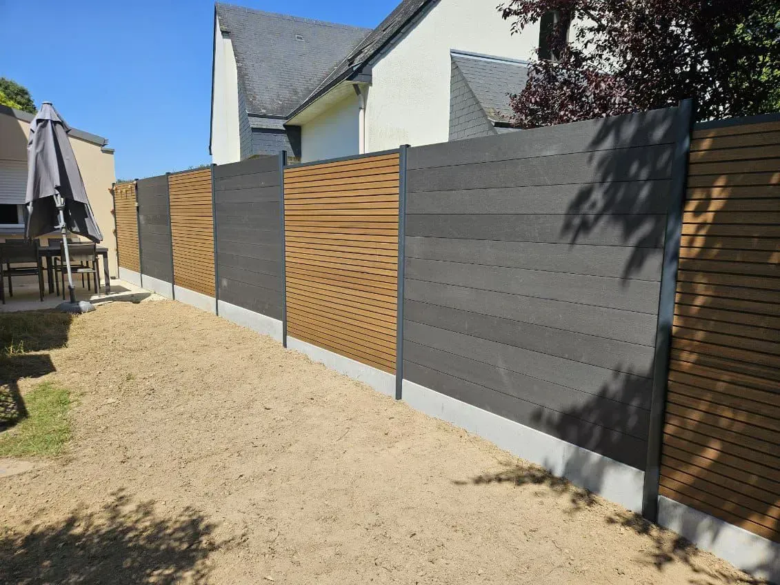 Clôture composite en bois et gris dans une cour contre une maison sous un ciel bleu.