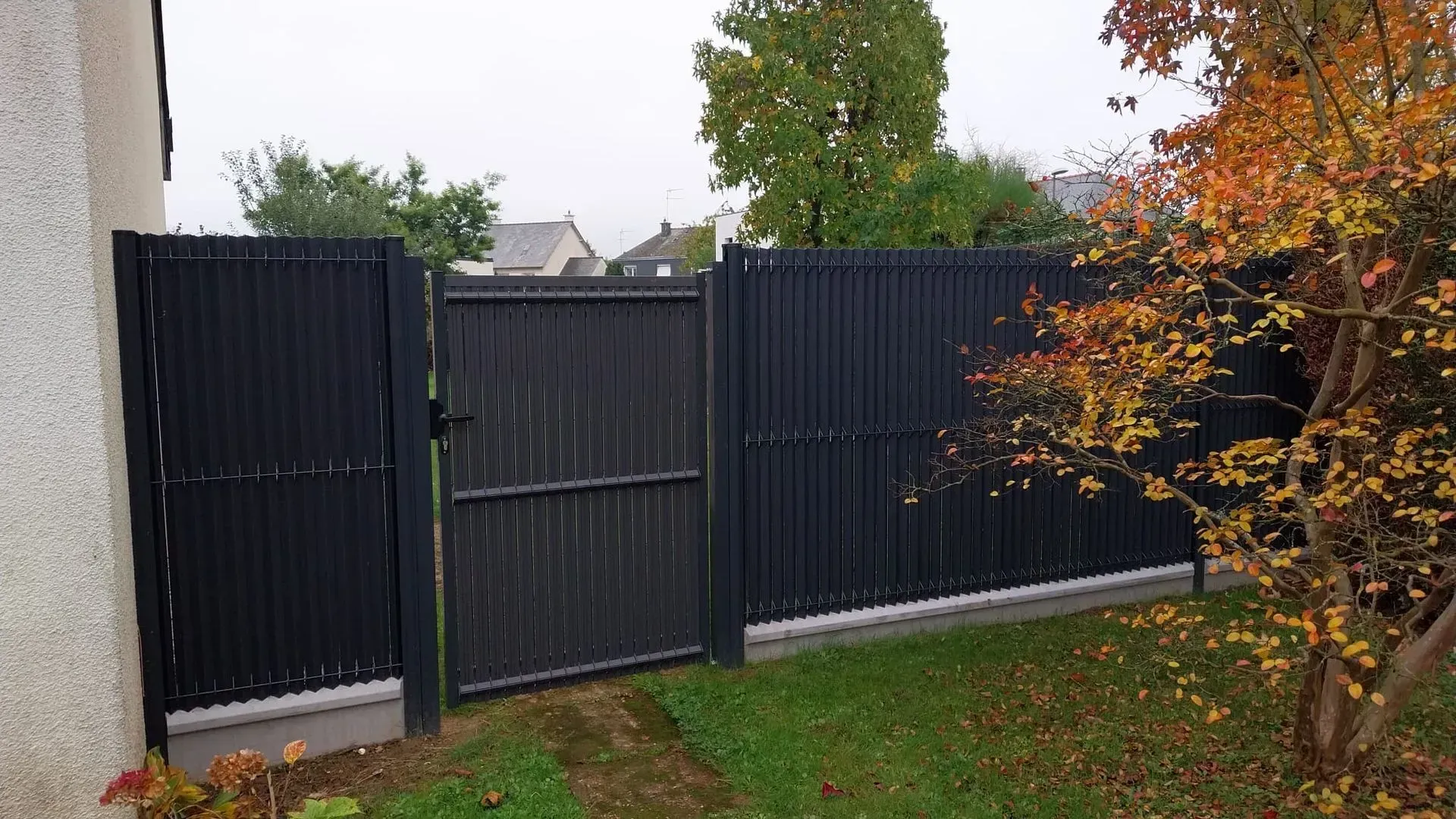 Clôture noire et portail dans une cour avec feuillage d'automne.