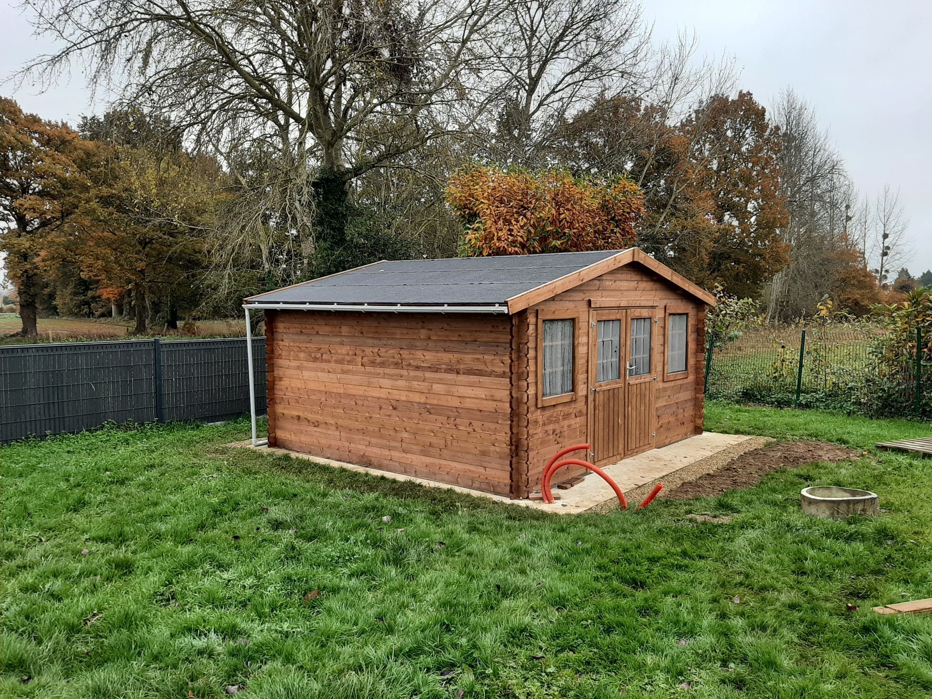 Abri en bois dans une cour avec des arbres d'automne en arrière-plan.