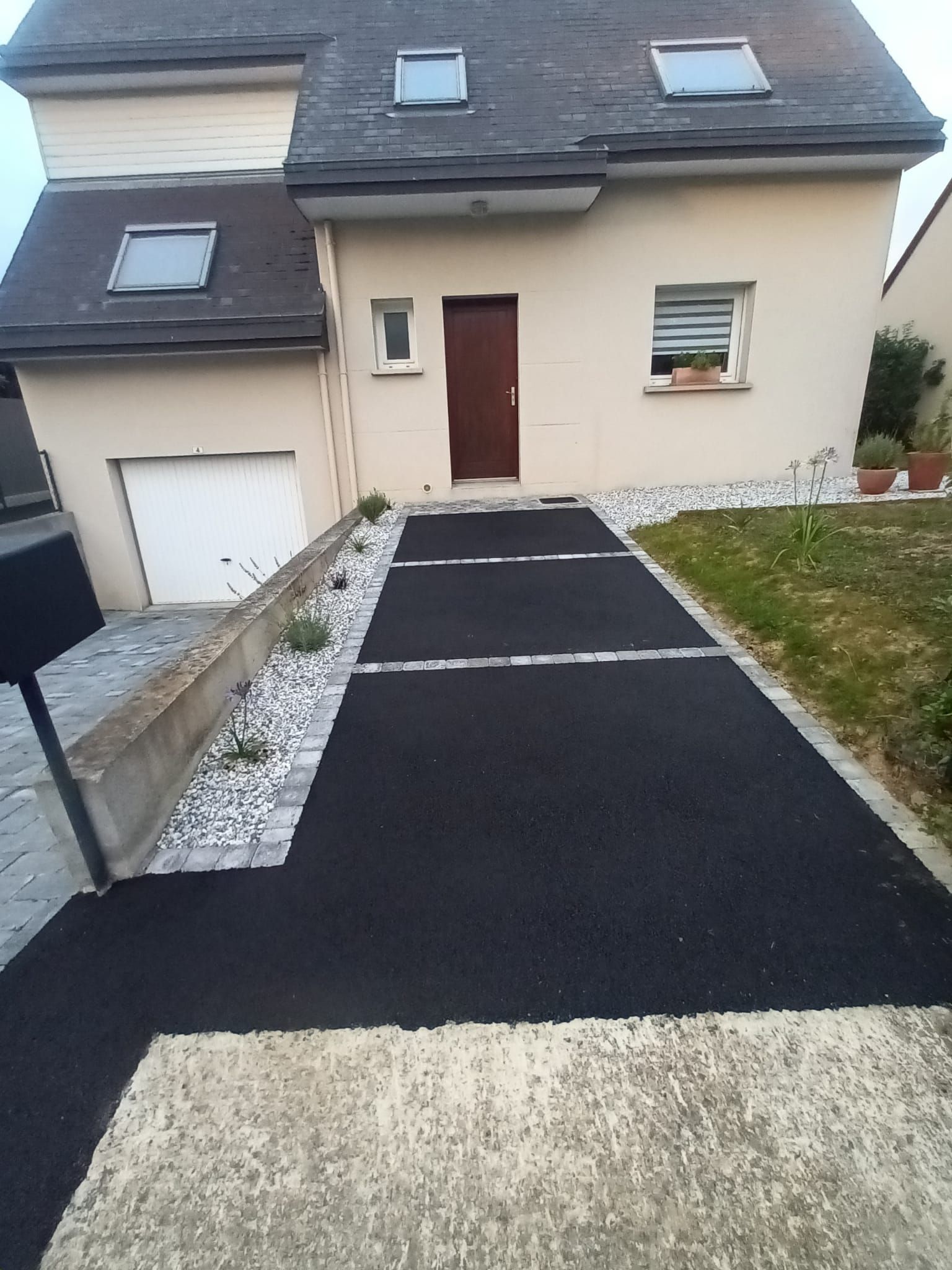 Une maison avec une allée noire nouvellement pavée et un extérieur de couleur claire.