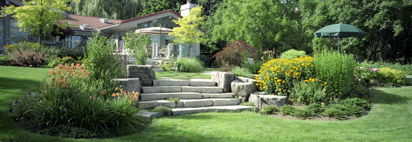 Des marches en pierre dans un jardin luxuriant avec des fleurs colorées, une pelouse verte et une pergola au-dessus