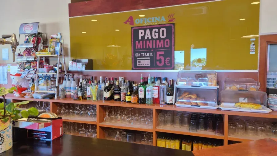 Mostrador de tienda con bebidas y aperitivos, cartel amarillo en la pared que dice “PAGO MÍNIMO 5€”