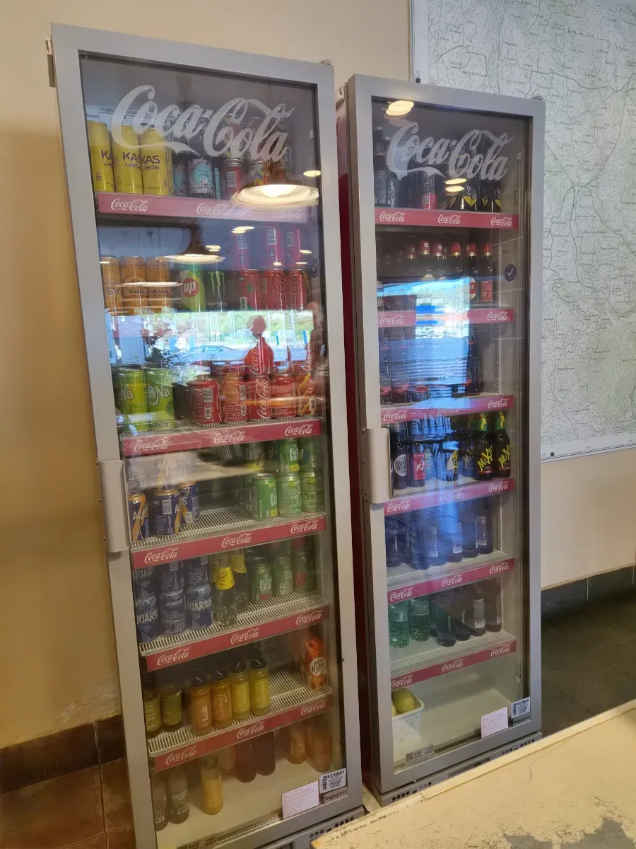 Dos refrigeradores de Coca-Cola con puertas de vidrio llenos de bebidas variadas en una esquina de la tienda.