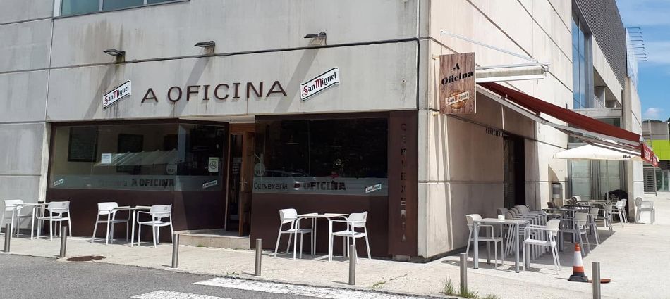 Exterior de la cafetería A Oficina con mesas al aire libre en una esquina soleada.