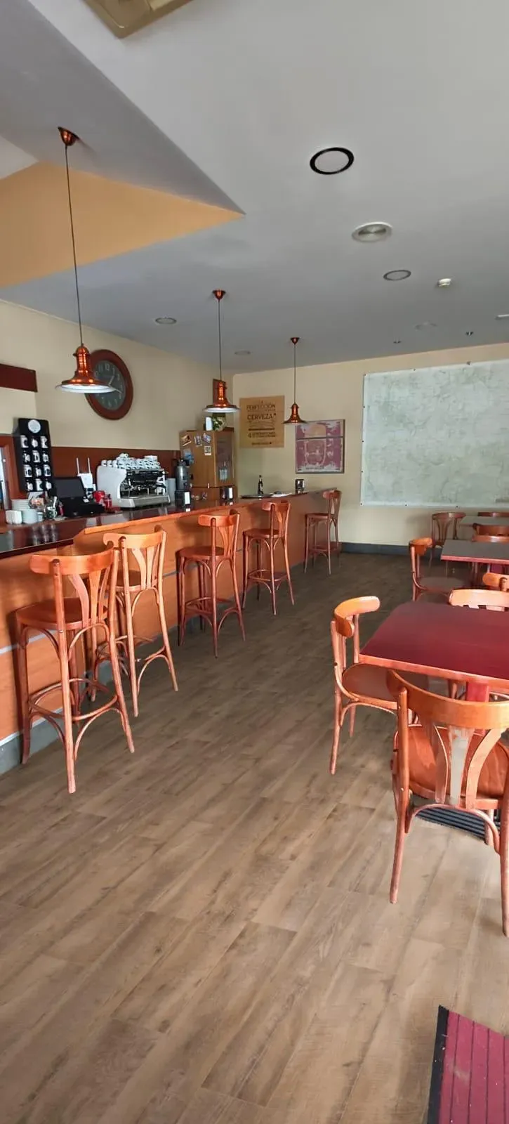 Interior vacío de una cafetería con suelo de madera, taburetes naranjas, mesas y una barra.