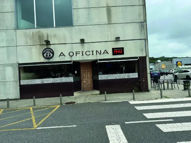 Fachada de la cafetería A Oficina con un letrero rojo, vista desde una calle con pasos de peatones señalizados.