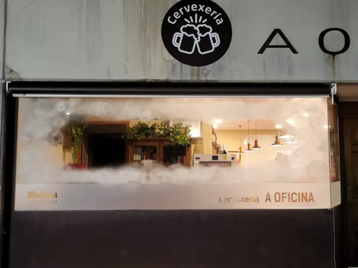 Escaparate con un escaparate iluminado y un letrero que dice “A OFICINA” por la noche.