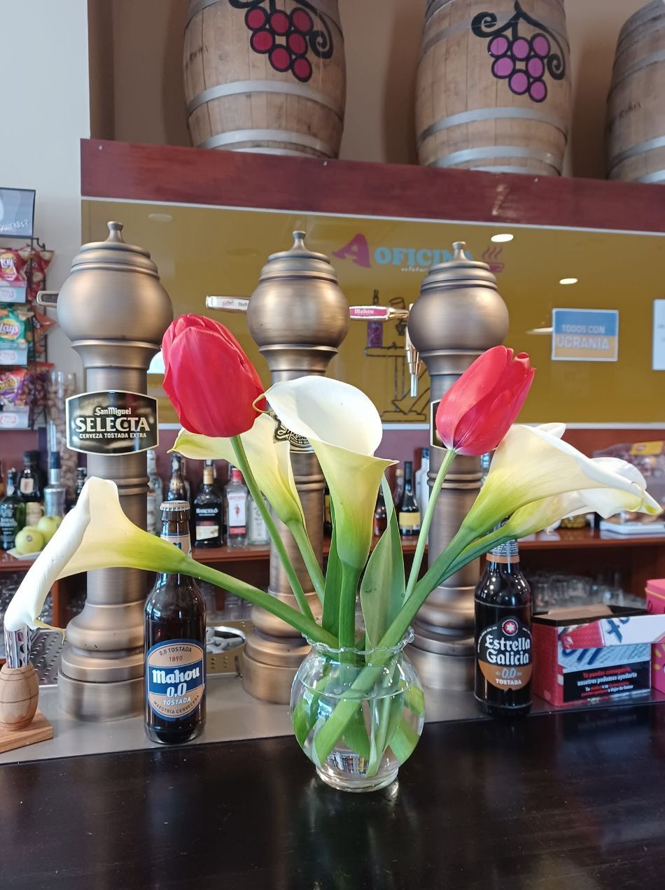 Jarrón de cristal con calas rojas y blancas sobre la barra de un bar, con botellas de licor al fondo.