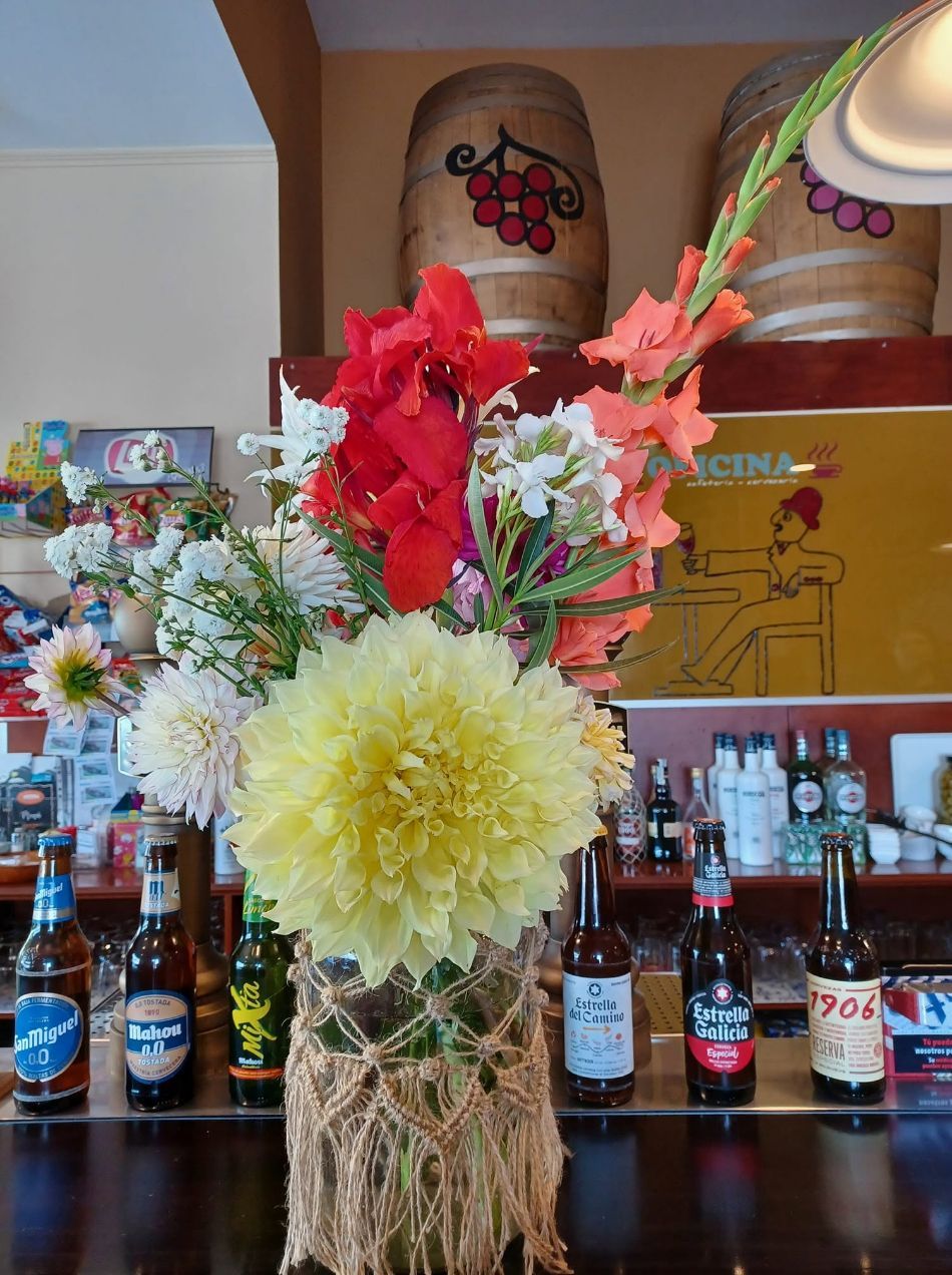 Ramo de flores con flores rojas, rosas y amarillas sobre la barra de un bar, con botellas y elementos decorativos al fondo.