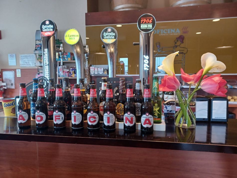 Varias botellas de cerveza alineadas en la barra junto a grifos y flores.