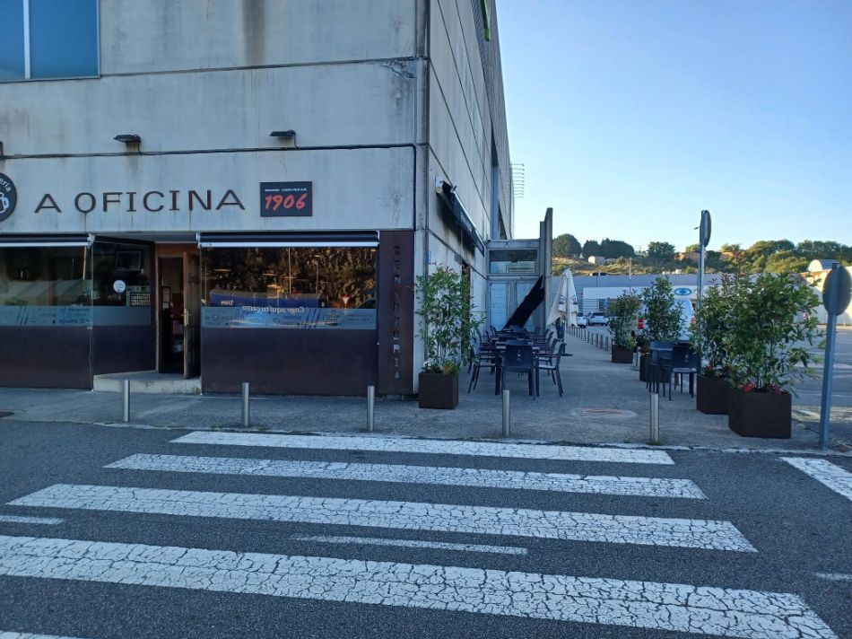 Local comercial con paso de cebra, asientos al aire libre y plantas en macetas a lo largo de una soleada esquina.
