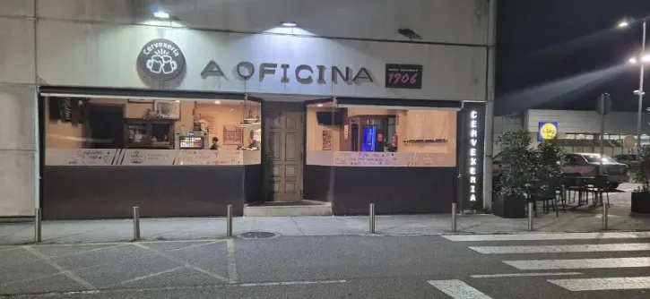 Vista nocturna de la fachada del restaurante Oficina con ventanas y letreros iluminados.