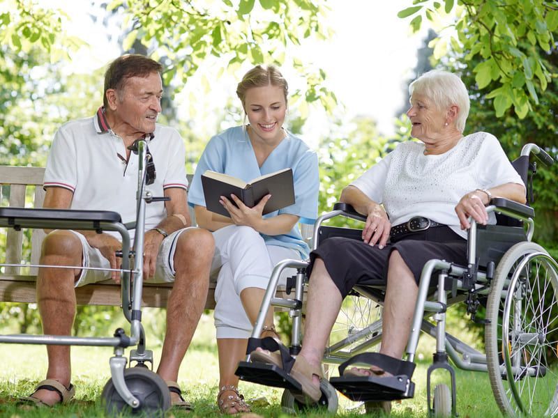 Eine Krankenschwester liest einem Paar im Rollstuhl ein Buch vor | Ambulanter Pflegedienst Rotenburg