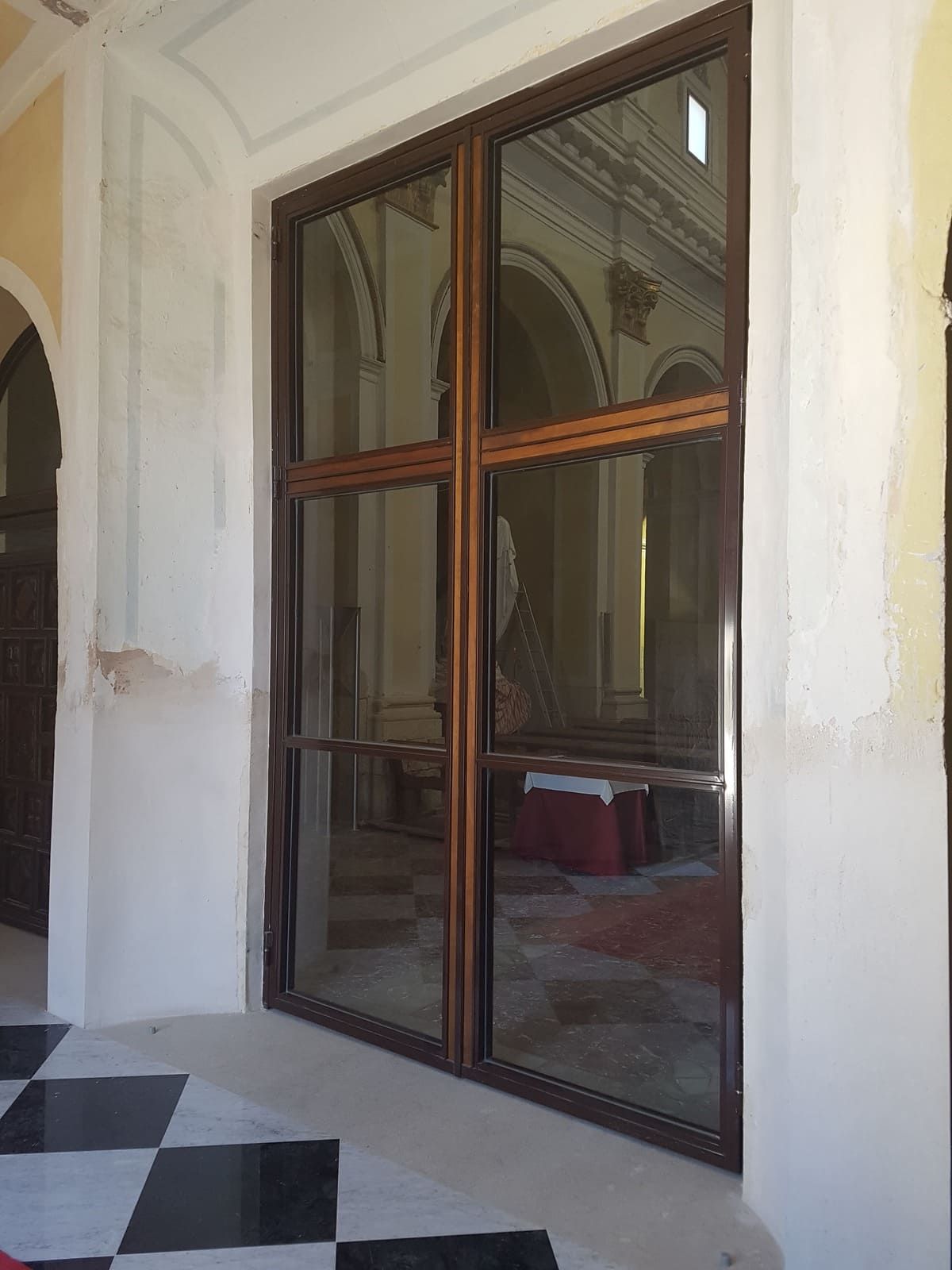 Puerta corredera de cristal con marco de madera oscura en un pasillo blanco con suelo de baldosas blancas y negras.