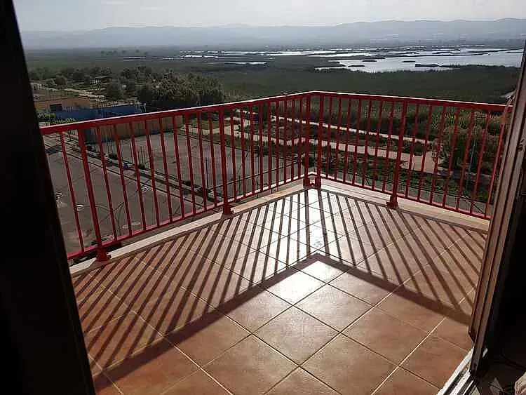 Balcón con barandilla roja y suelo de baldosas, con vistas al lago y las colinas a lo lejos.