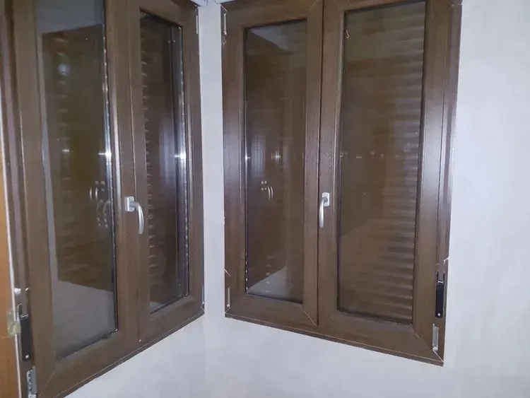 Ventanas de madera marrón en una esquina, vistas desde el interior de una habitación con paredes blancas.