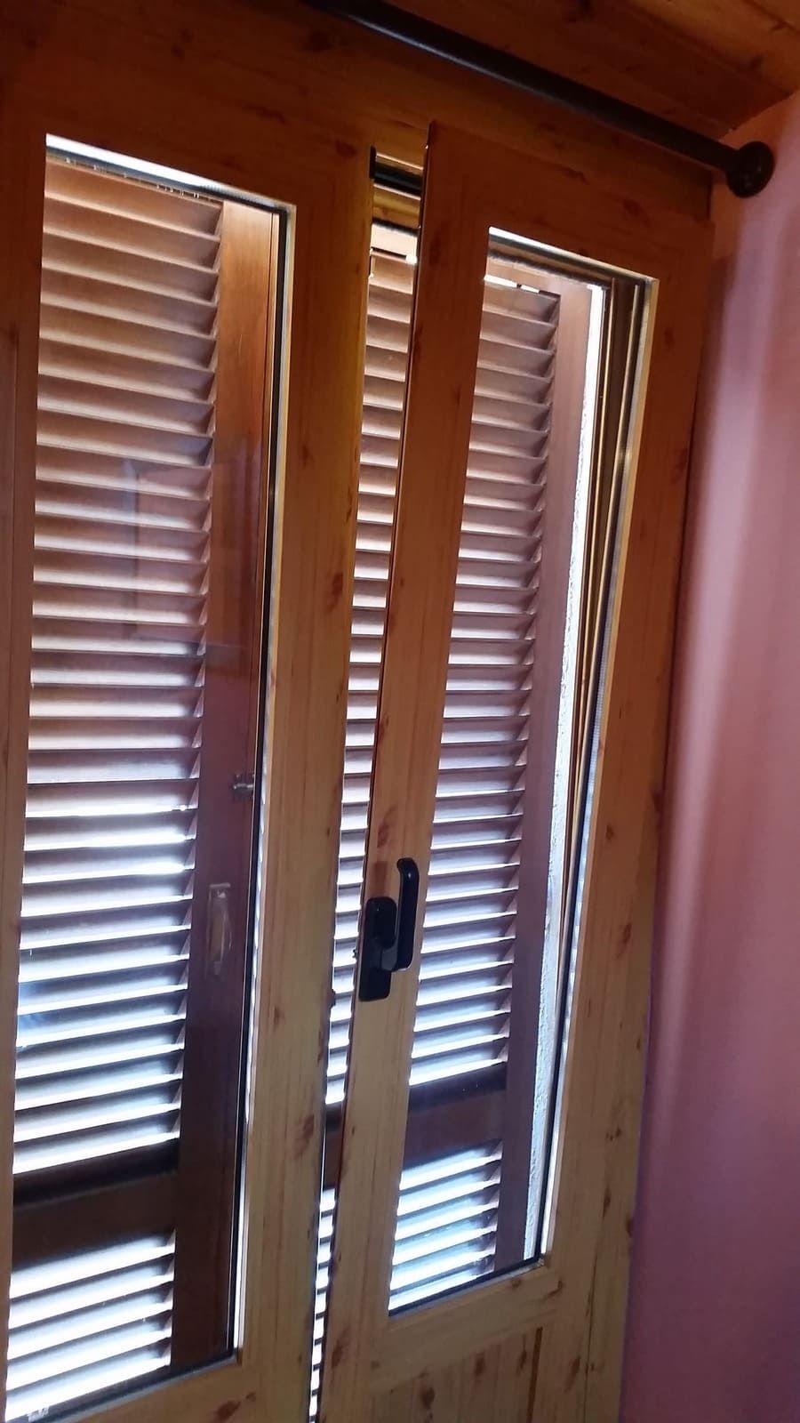 Puertas francesas de madera con contraventanas blancas y tirador negro en una habitación con iluminación cálida.