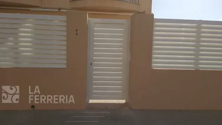 Puerta y portón beige cerrados con listones horizontales junto a un letrero que dice “LA FERRERIA”.