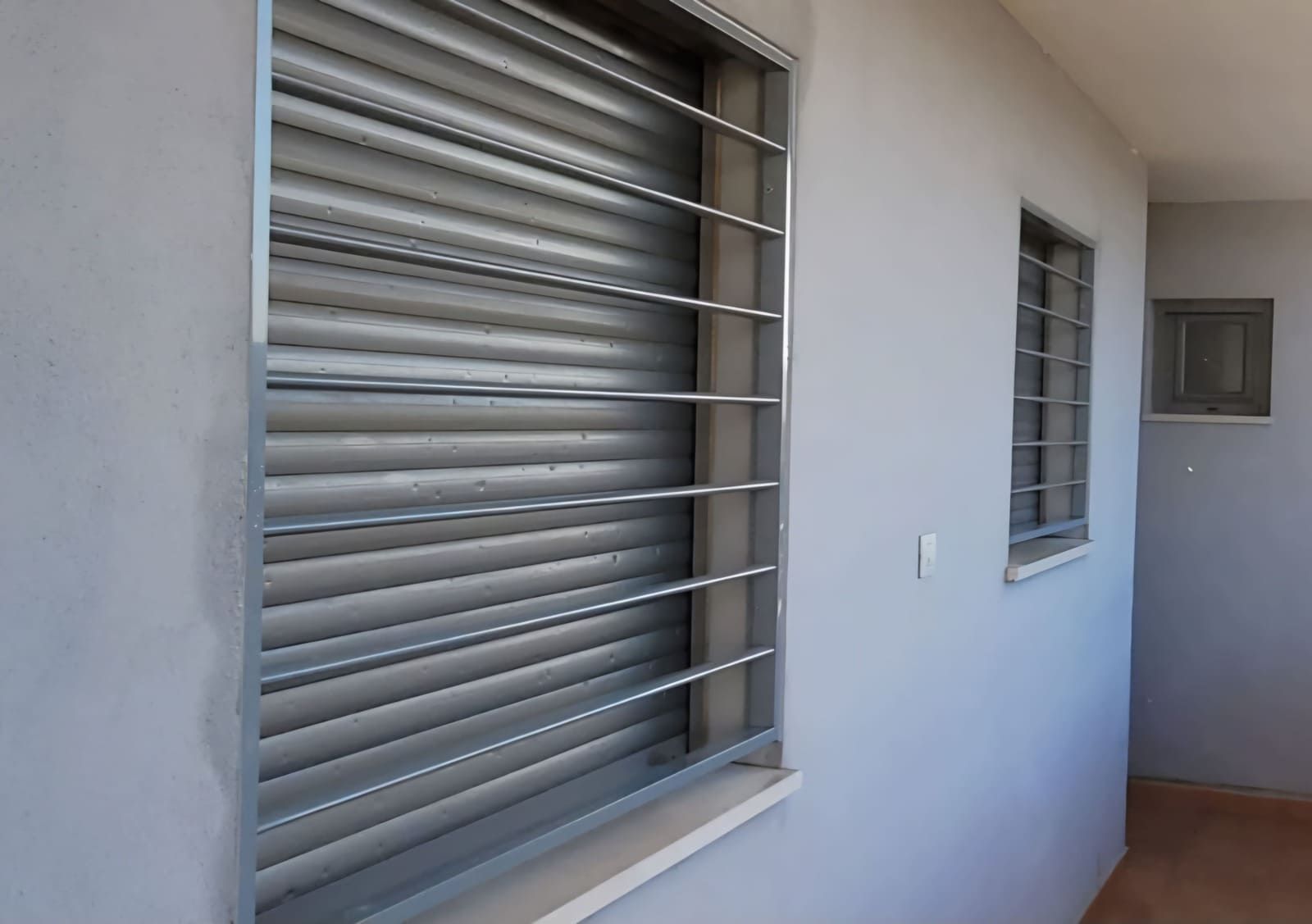 Pasillo con ventanas enrejadas y una pared blanca que conduce a una pequeña puerta con ventana al final.
