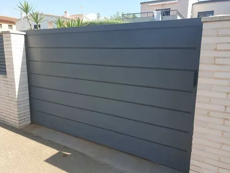 Puerta de entrada moderna de color gris entre pilares de ladrillo blanco en una zona residencial.